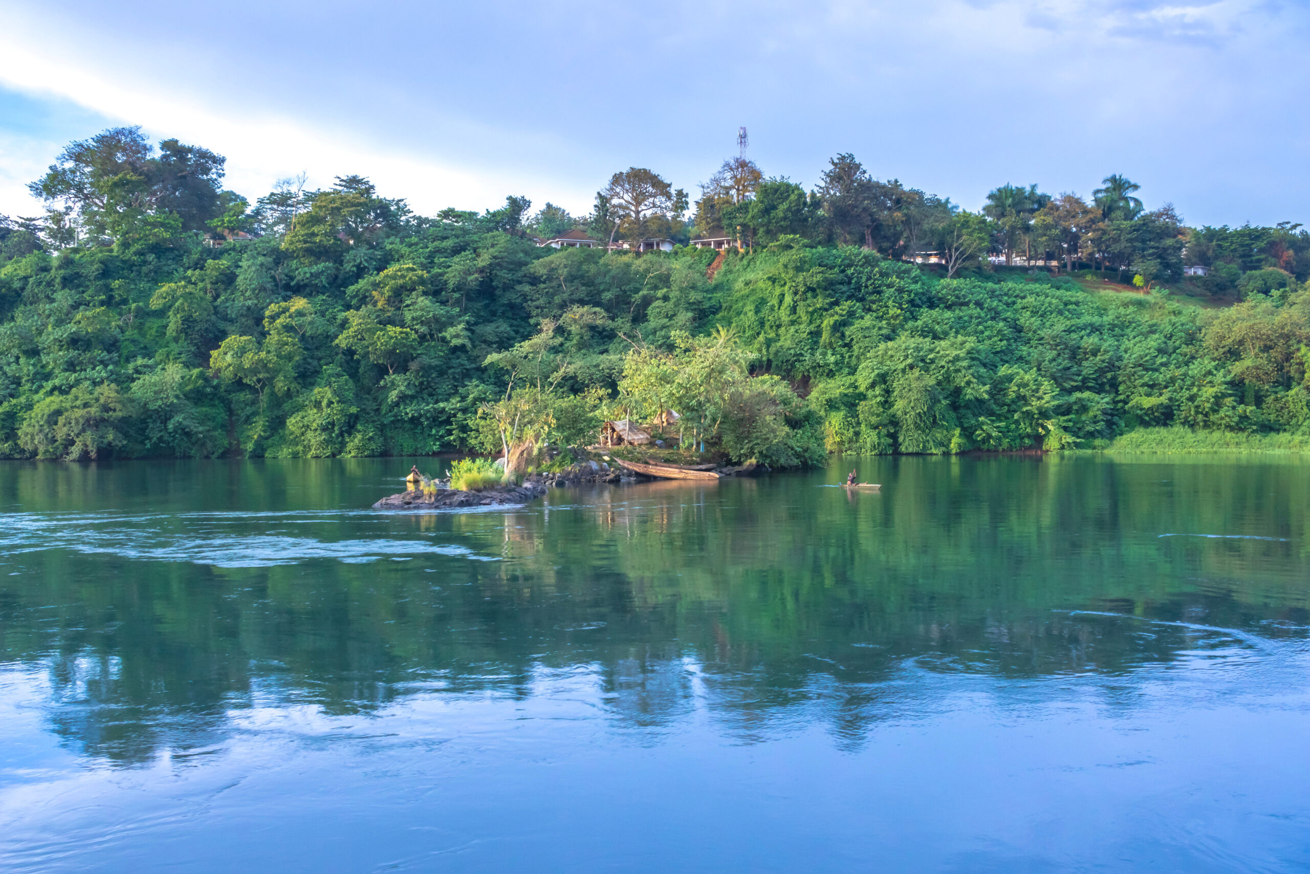 View of the fisherman in boats fishing on the Victoria Nile river, with trees growing and the reflections on the water, Jinja, Uganda, Africa